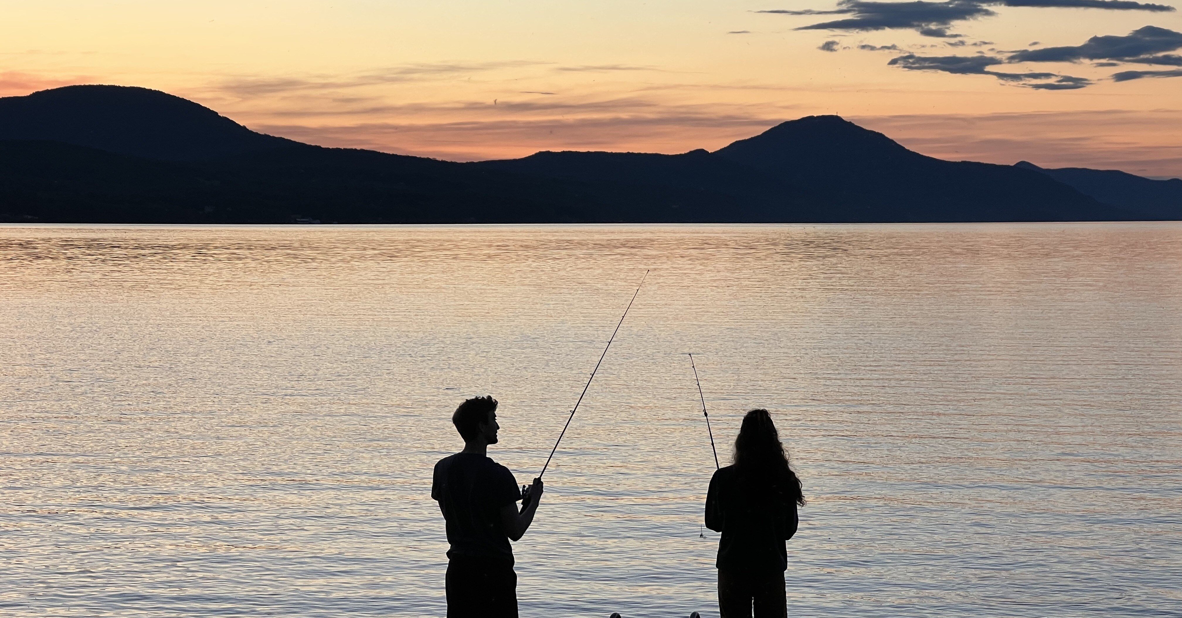  Two young adults fishing at sunset on lake memphremagog in vermont